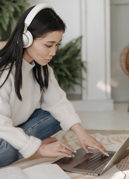 A woman wearing headphones is focused on her laptop screen
