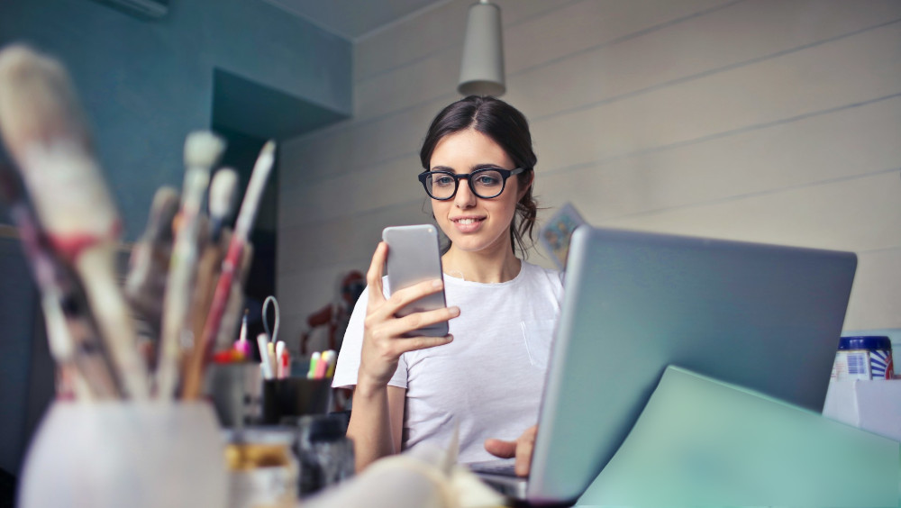 A woman working on a laptop and a smartphone at her desk