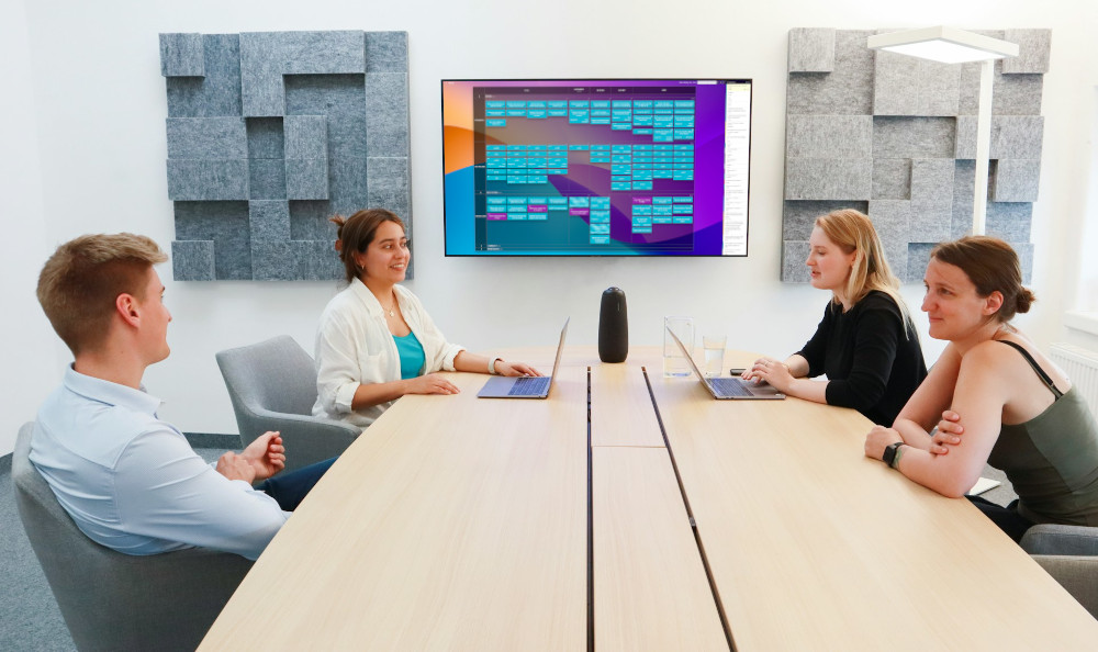 Team at a conference table with a Kanban Tool board casted to the tv screen