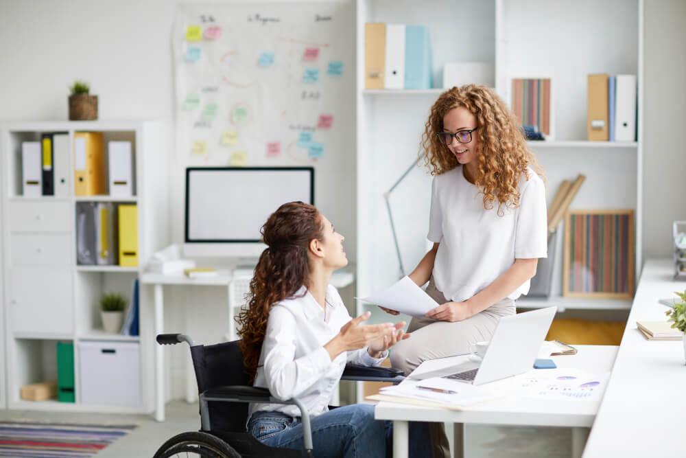 A woman is working at her desk while someone else is distracting her with some questions