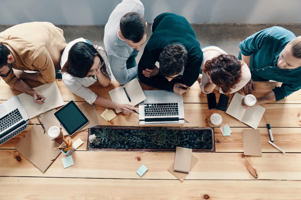 Several team members are gathered over a laptop screen in an office