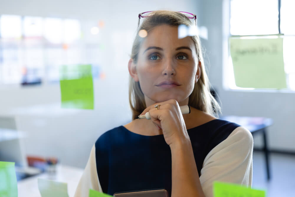 A woman looks at a glass door Kanban while planning the best way forward with a project