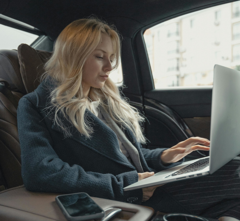 Businesswoman appearing cold and stern typing on a laptop in the back of a car