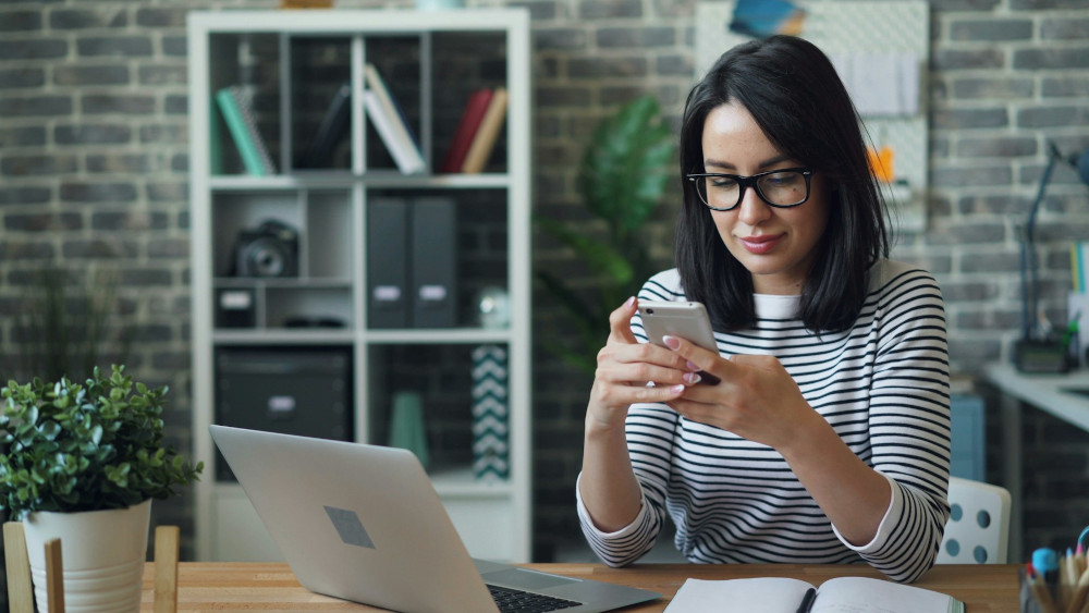 A woman working at a desk with a laptop and a smartphone