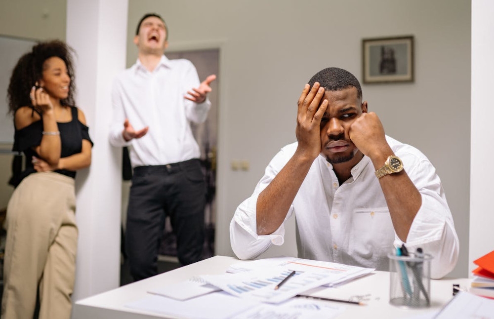 A man at a desk appears unmotivated while his colleagues stand idly in the background