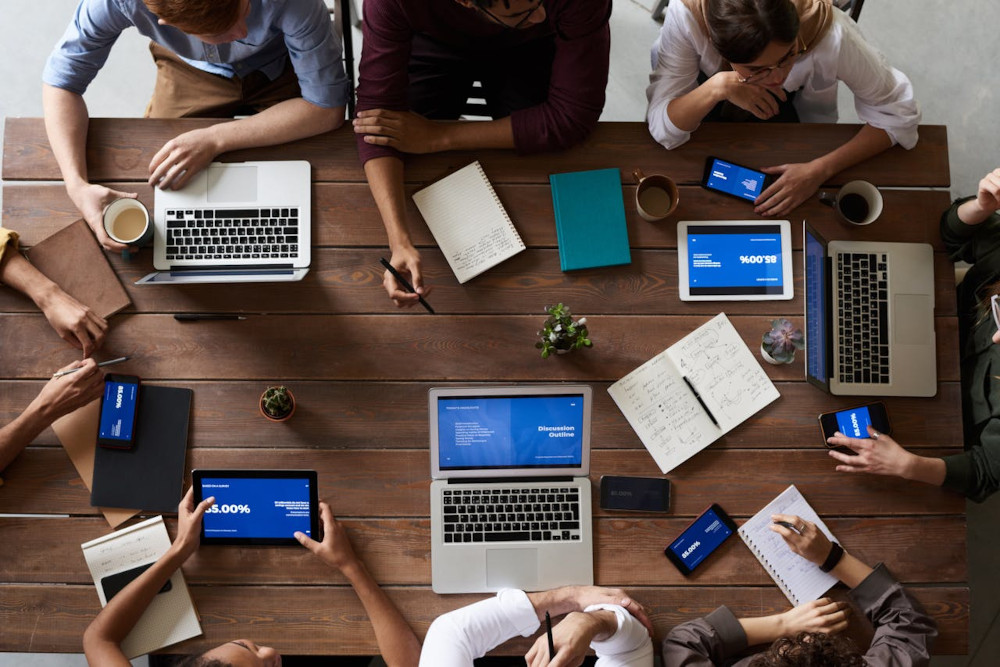 Kanban streamlines communication and reduces meetings Team in a meeting at a conference table with laptops and smartphones