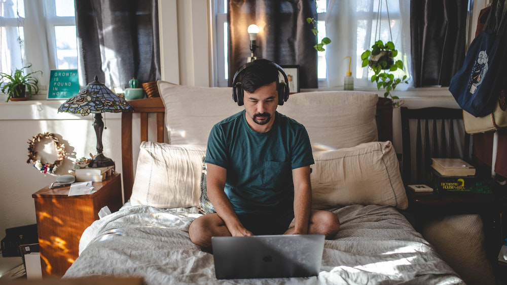 A man works on a laptop from his bedroom
