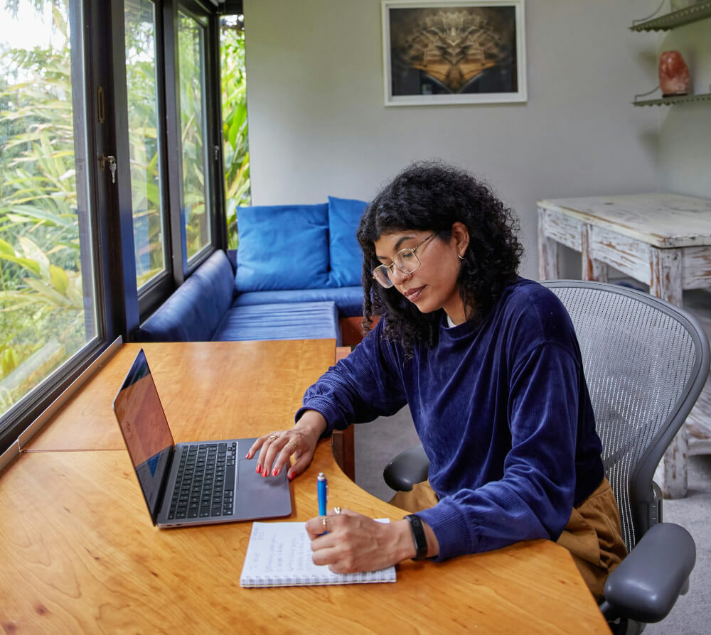 A woman checks off a list while looking at a laptop screen